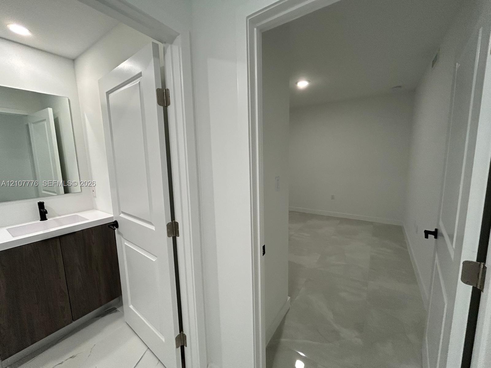 Vanity featuring dark wood-finish cabinetry, a rectangular sink, and a matte black faucet, paired with large-format stone-finish floor tile and interior doors with matte black hardware