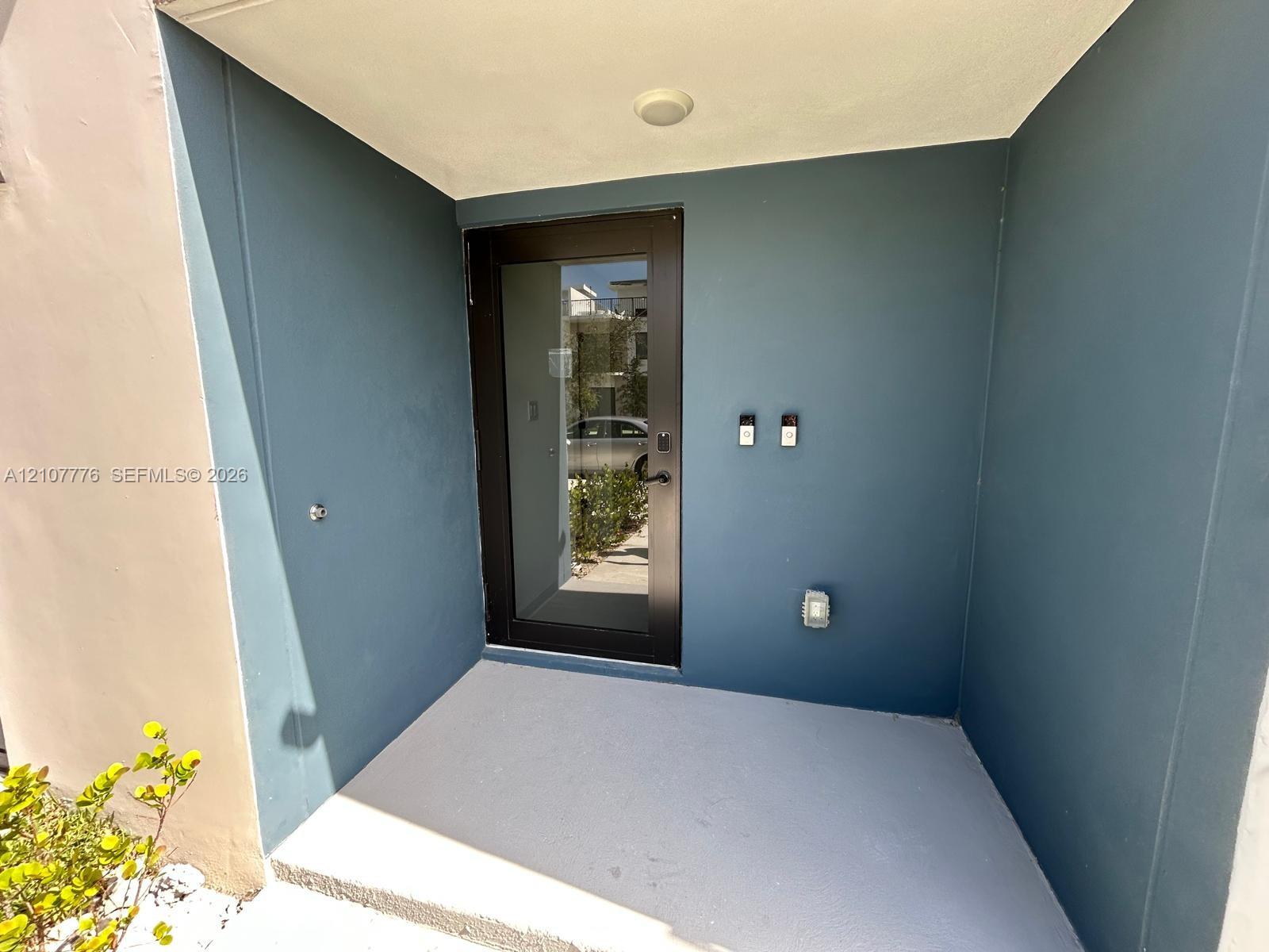 Covered entryway featuring a modern black-framed glass door, smooth-finish exterior walls, and a light-toned concrete porch surface