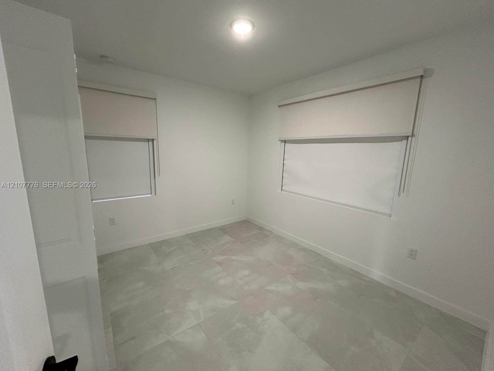 Neutral interior featuring large-format tile flooring, crisp white walls, and dual windows equipped with roller shades