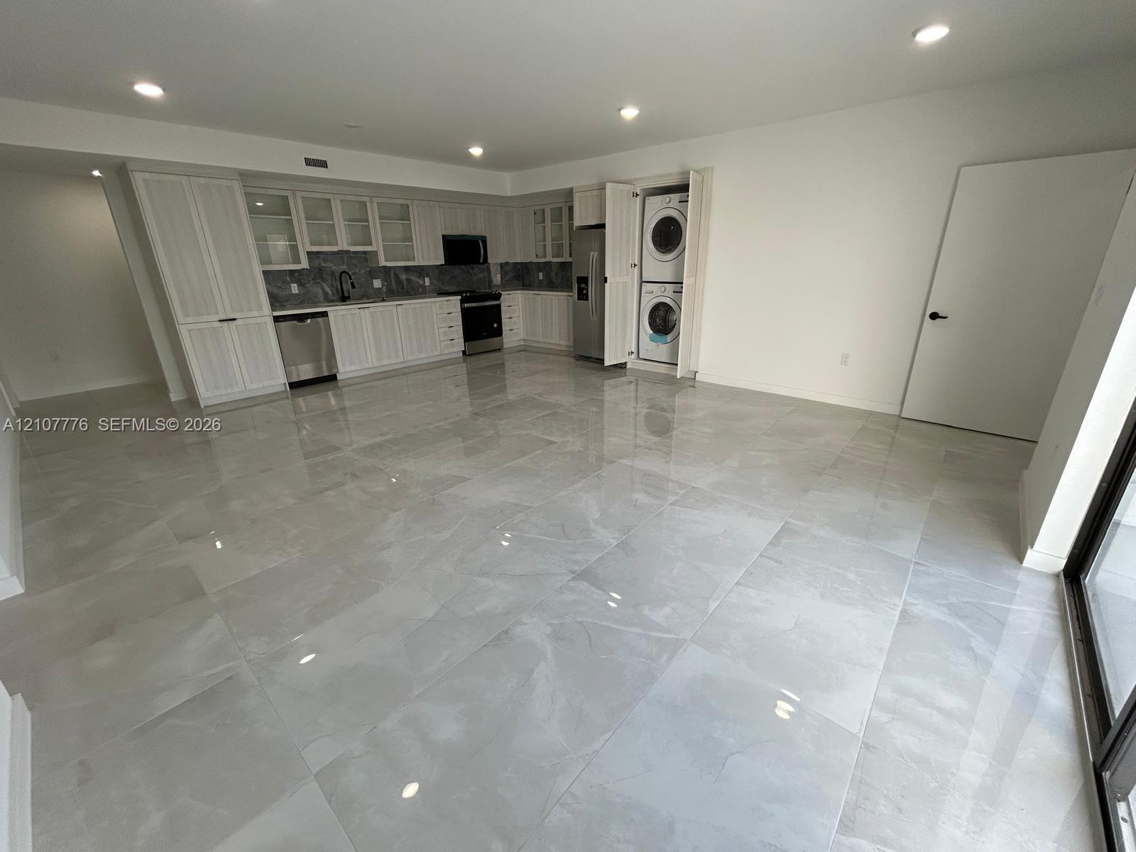 Large-format tile flooring, white cabinetry with integrated upper glass-front displays, stone-finish backsplash, stainless steel appliances, and built-in stacked laundry