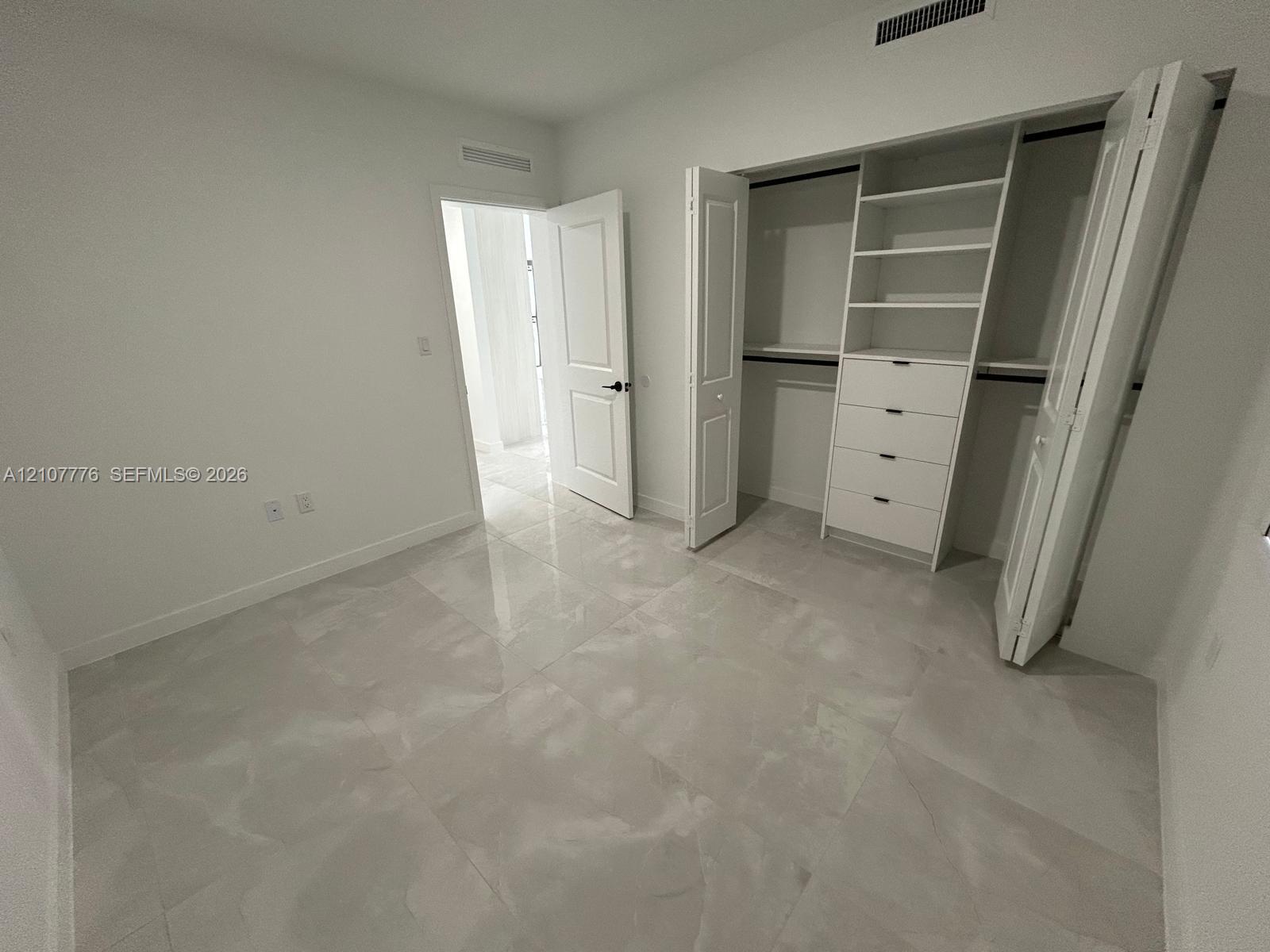 Room featuring large-format tile flooring, a custom walk-in closet with built-in shelving and drawers, and panel-style interior doors