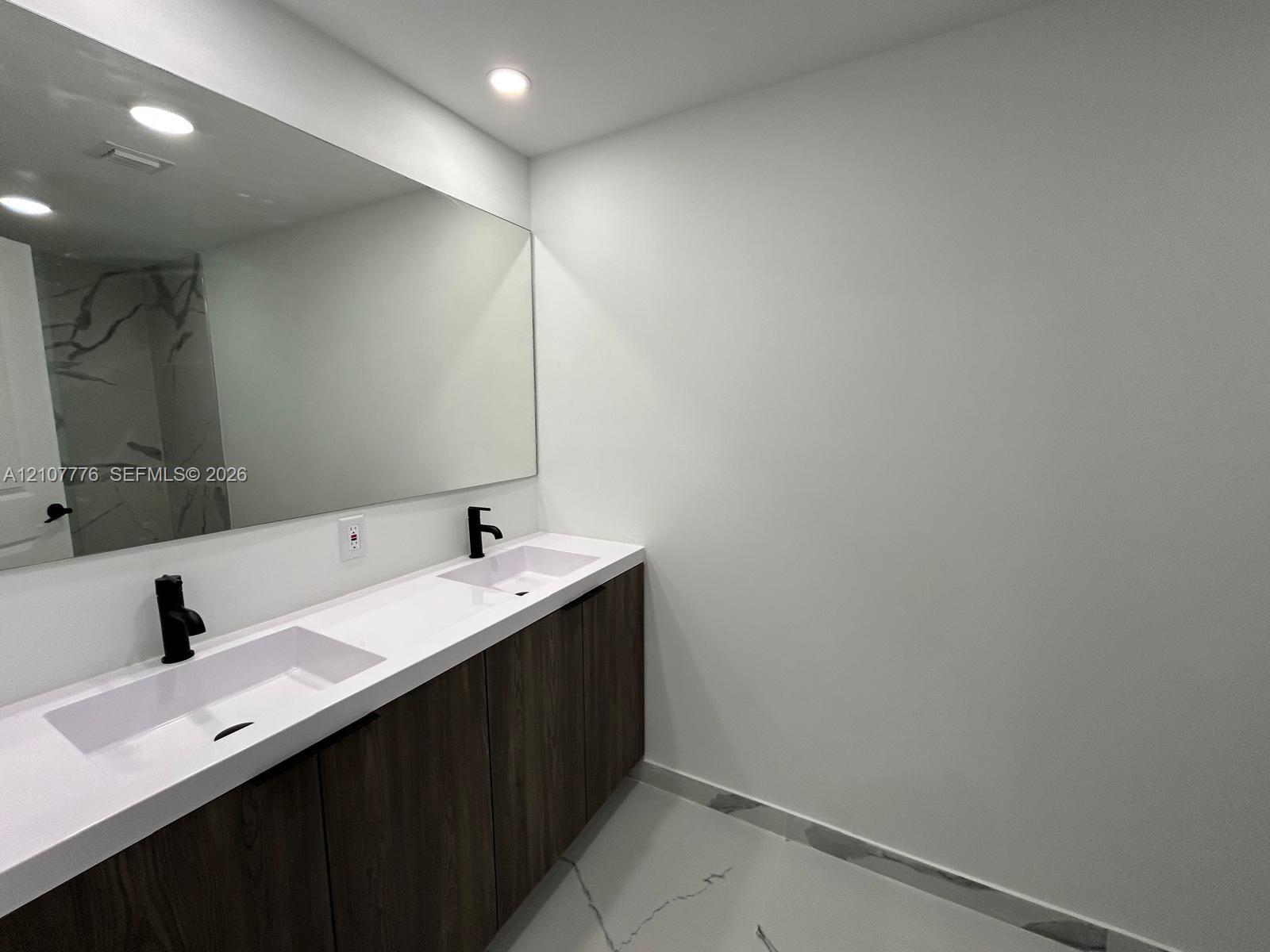Dual-sink vanity with matte black fixtures, quartz countertop, wood-finish cabinetry, full-width mirror, and large-format porcelain floor tile