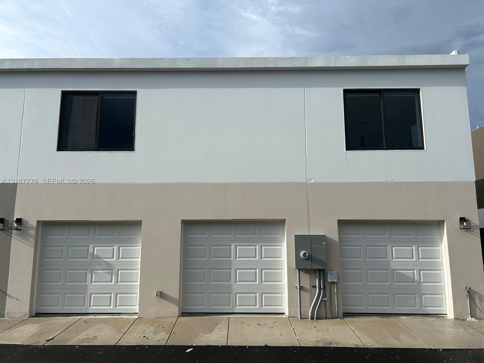 Multi-level exterior featuring a two-tone stucco facade, three white sectional garage doors, and sliding windows with black frames