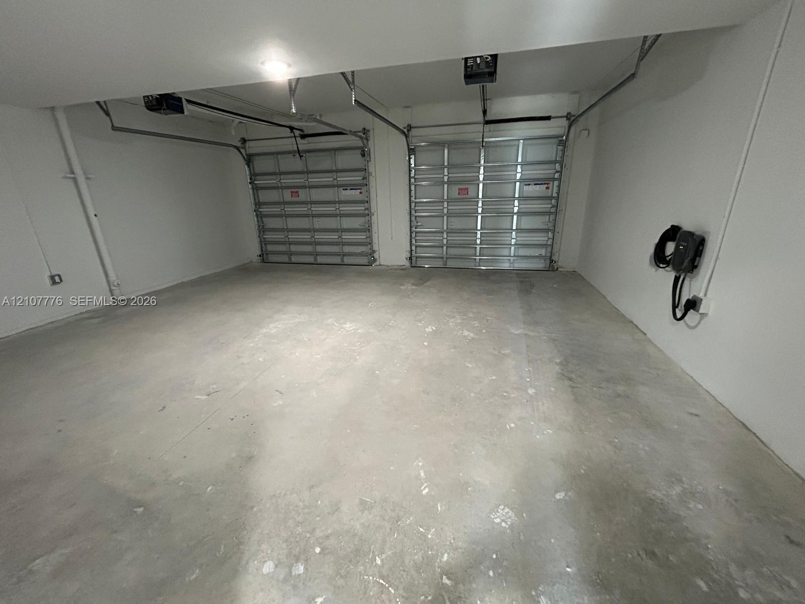 Two-car garage featuring dual sectional overhead doors, concrete flooring, and a wall-mounted electric vehicle charging station