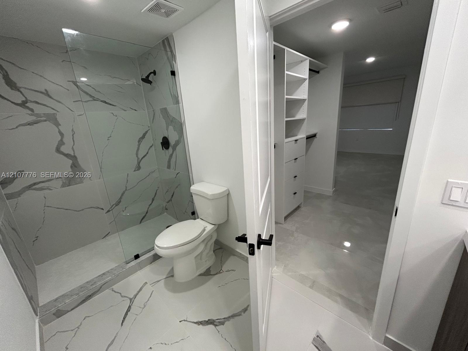 Walk-in shower featuring glass paneling, floor-to-ceiling stone-look tiling, and matte black fixtures, paired with a custom built-in closet system including shelving and drawer storage