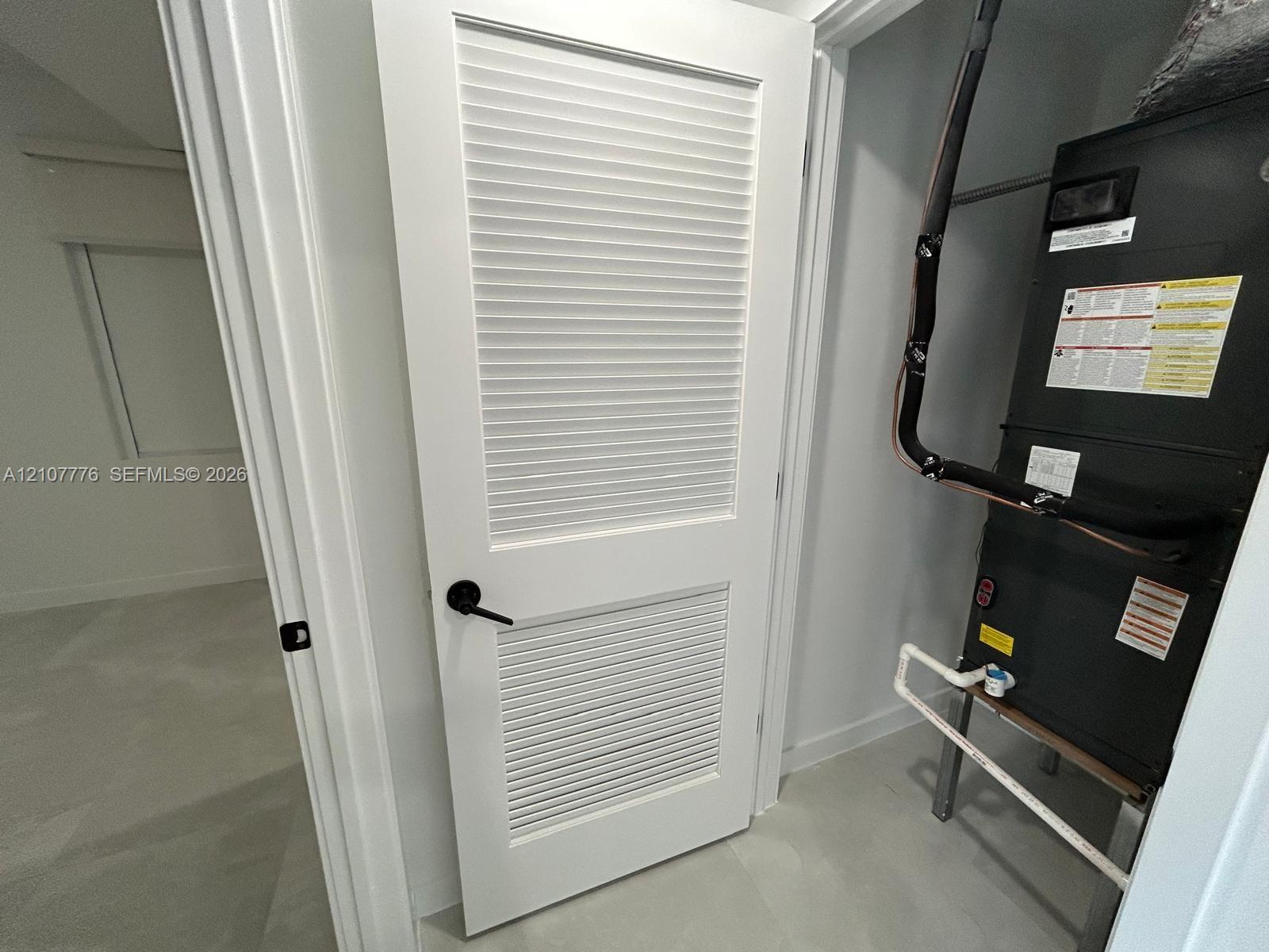 Utility closet featuring a white louvered door with matte black hardware and an installed mechanical furnace unit