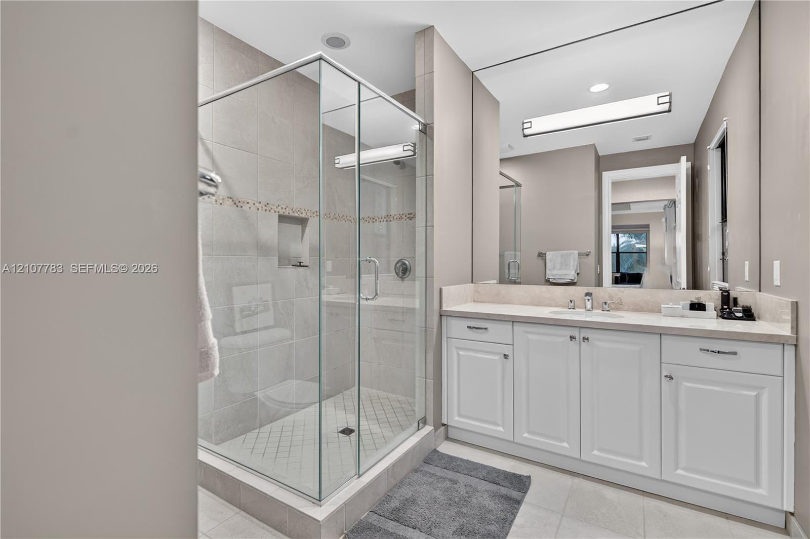 Walk-in glass shower with tile surround, white cabinetry, integrated sink, stone-finish countertop, and large vanity mirror