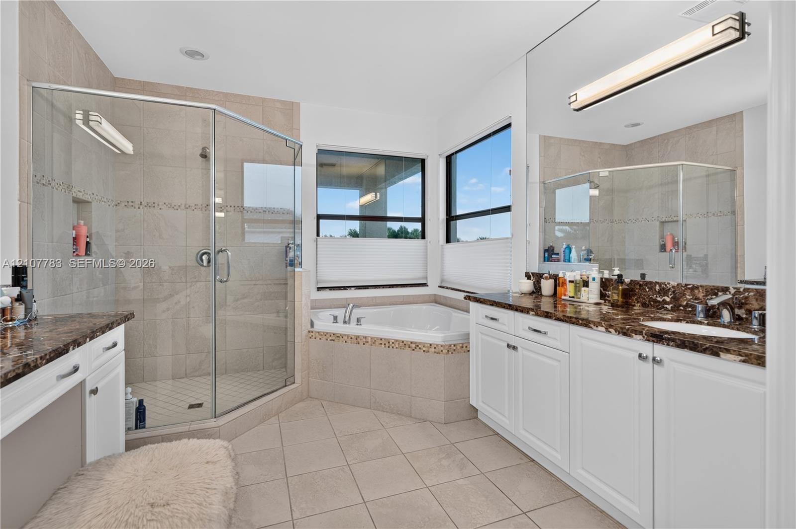 Bathroom featuring a double vanity with stone countertops, a corner soaking tub, and a glass-enclosed shower with tiled surround