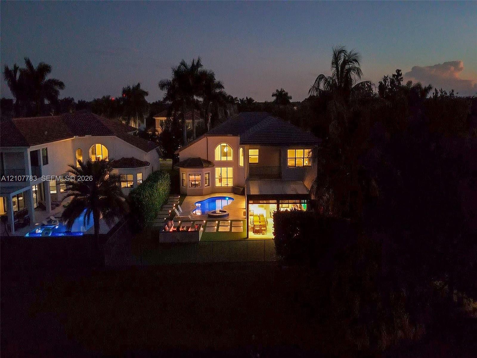Rear exterior featuring an in-ground swimming pool, stone-paver pool deck, covered patio, and manicured landscaping with mature palm trees