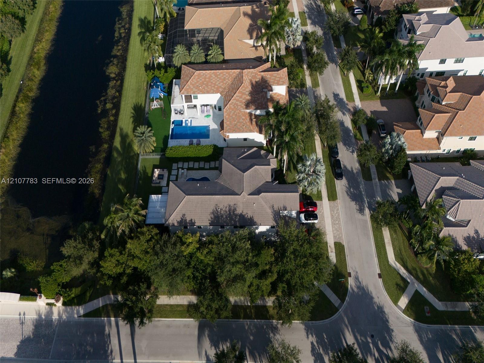 Aerial perspective of a waterfront property featuring a multi-pitched tiled roof, private swimming pool, concrete paver patio, and professional landscaping