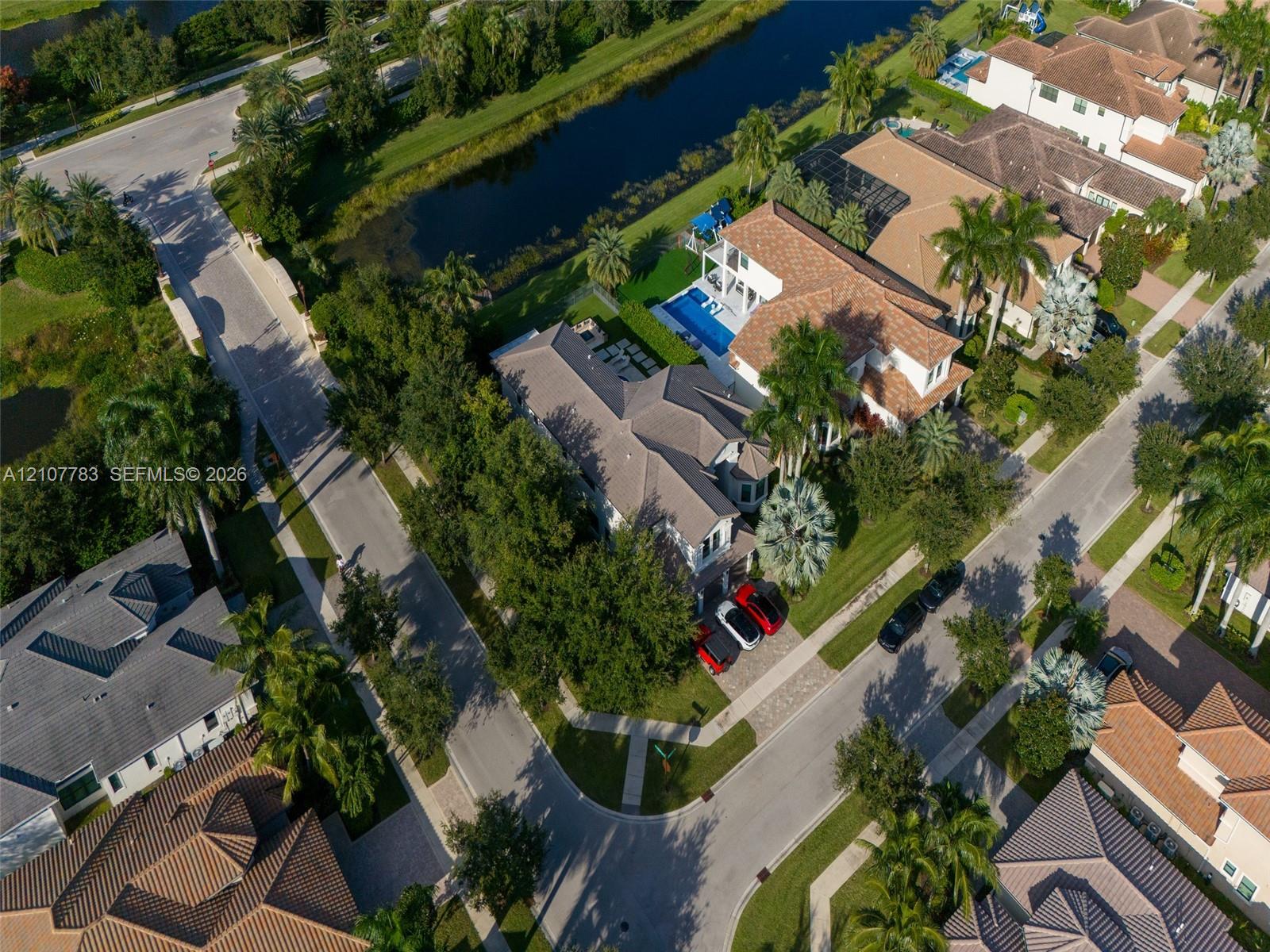 Aerial perspective featuring a multi-story residence with a tiled roof, an in-ground swimming pool, and a waterfront position