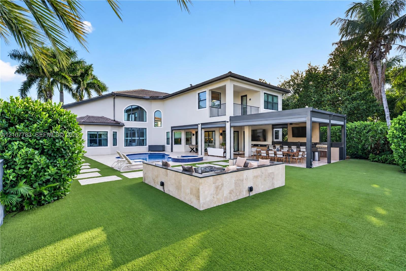 Rear exterior featuring a swimming pool, integrated spa, covered patio with outdoor kitchen, and stone-clad fire feature Rear exterior featuring a swimming pool, integrated spa, covered patio with outdoor kitchen, and stone-clad fire feature