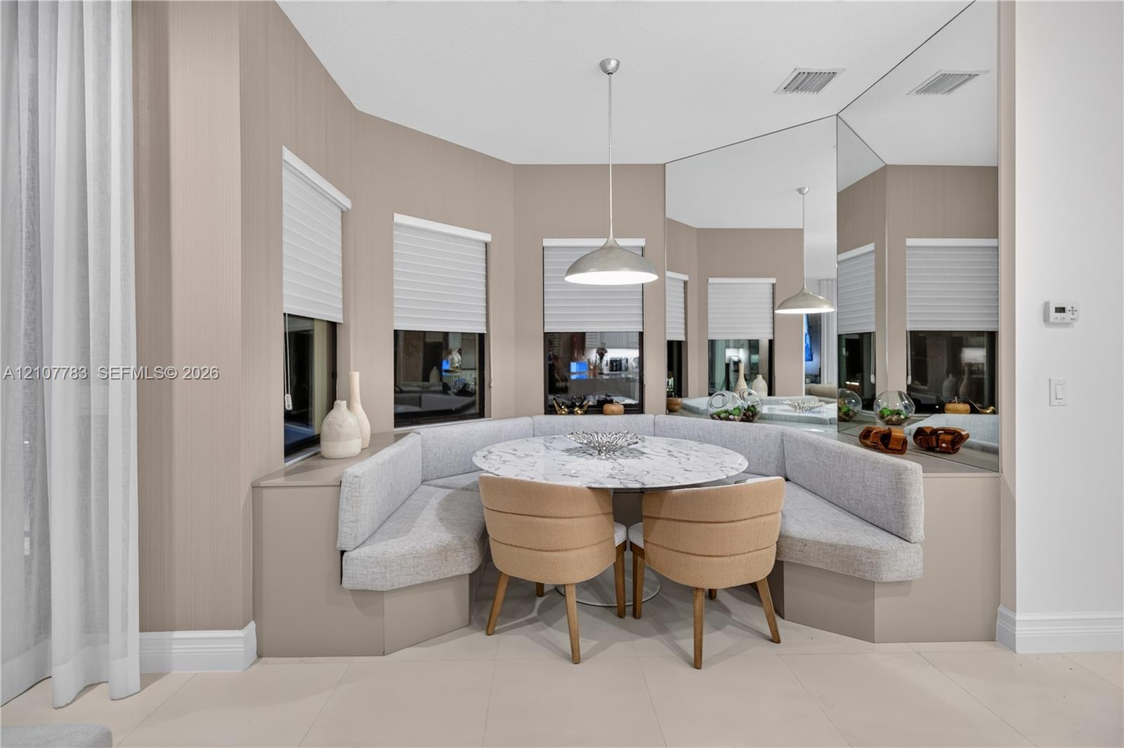 Custom built-in upholstered banquette seating, floor-to-ceiling wall mirror, bay window configuration with integrated blinds, and polished pendant lighting