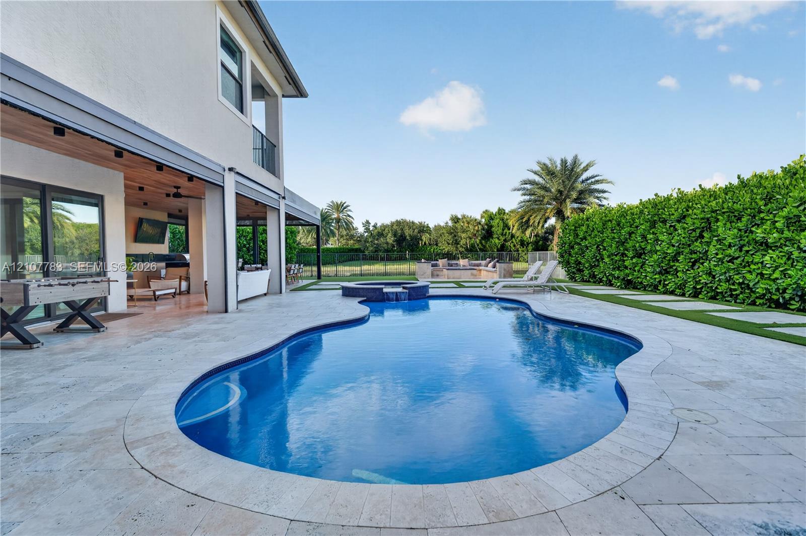 Outdoor living area featuring a covered patio, freeform swimming pool with an integrated spa, stone paver decking, and a built-in fire pit