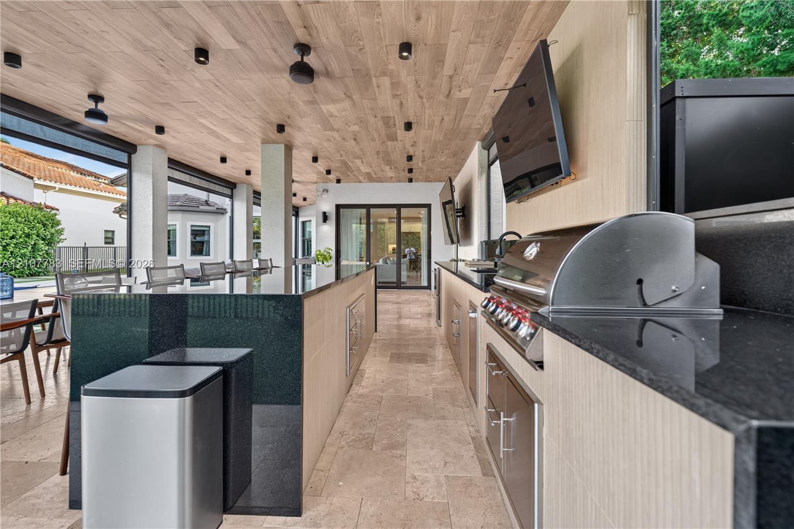 Outdoor kitchen featuring a stone-tile floor, wood-finish ceiling, dark stone countertops, integrated stainless steel grill, and recessed lighting