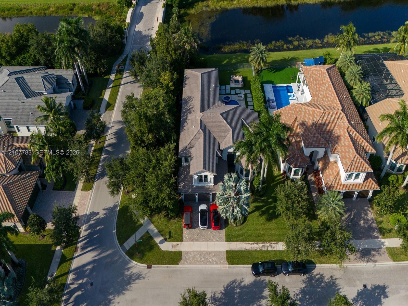 Aerial view featuring a multi-gabled roofline, paver driveway, mature landscaping, in-ground pool, and hardscaped patio area