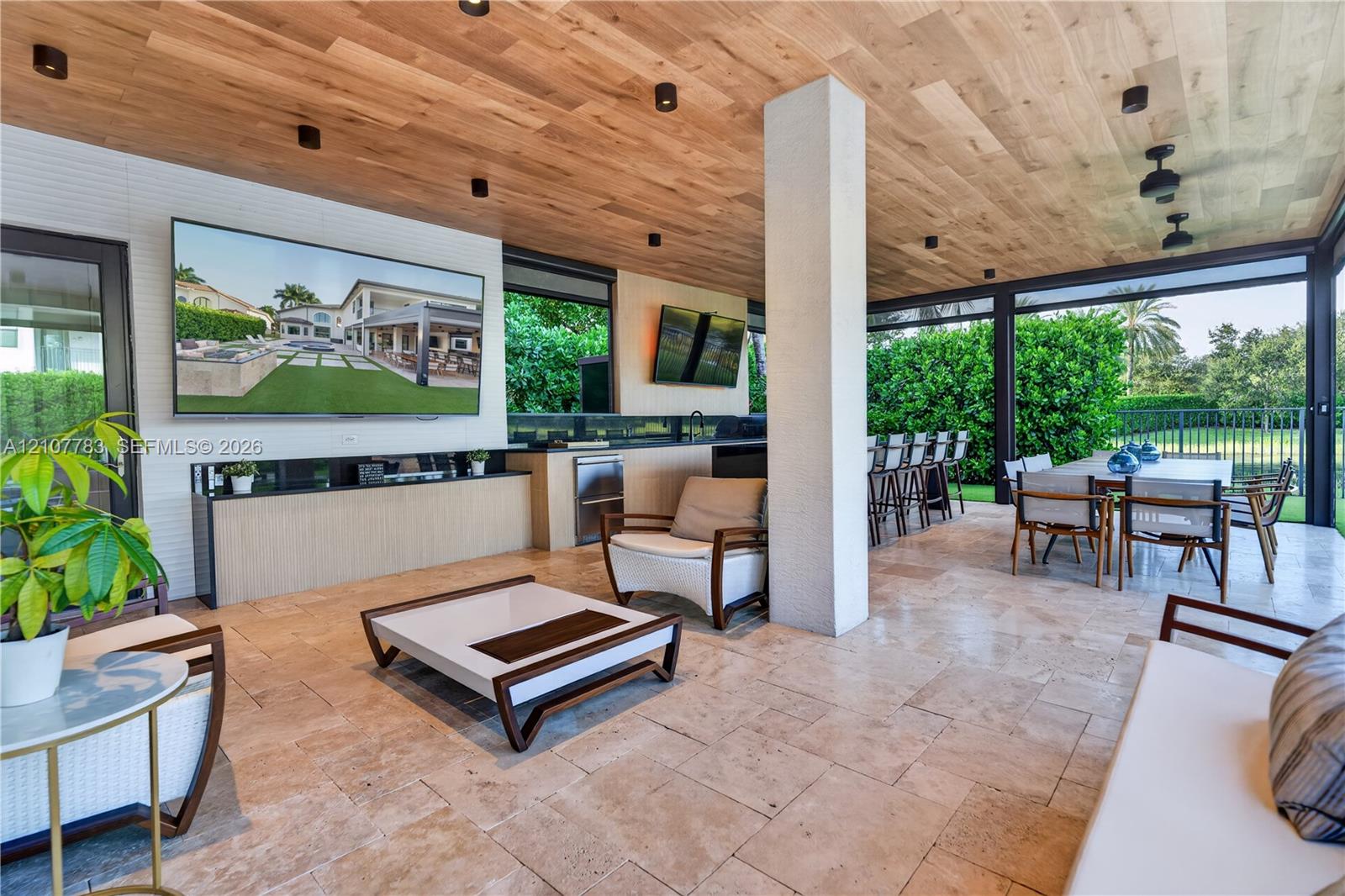 Covered outdoor living space featuring natural stone flooring, wood-plank ceiling, recessed lighting, and a built-in outdoor kitchen with stone countertop