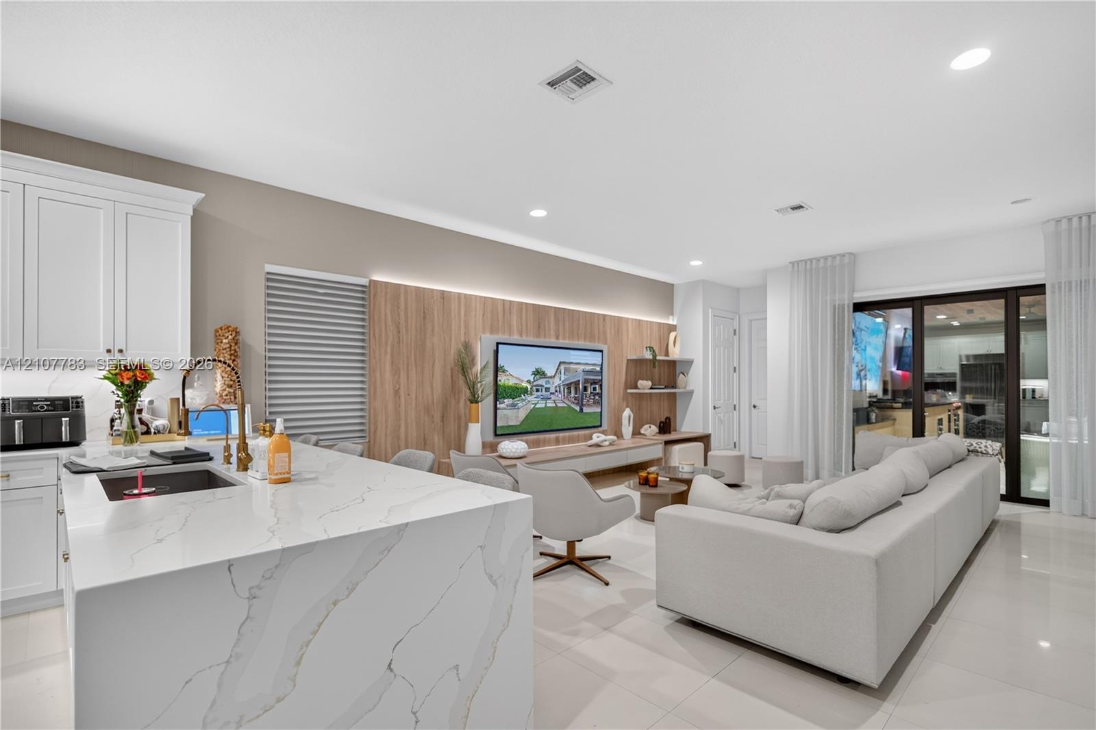 Kitchen featuring a waterfall-edge island with a stone-finish countertop, white cabinetry, integrated under-cabinet lighting, and large-format tile flooring