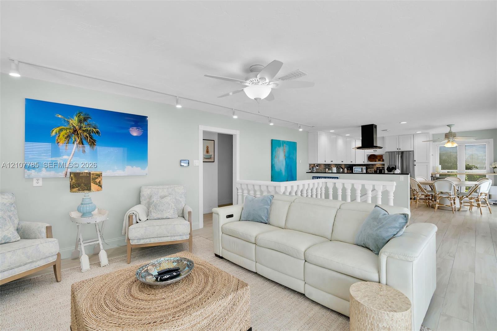 Open-concept interior featuring wood-finish flooring, white cabinetry, track lighting, ceiling fans, and balustrade railing