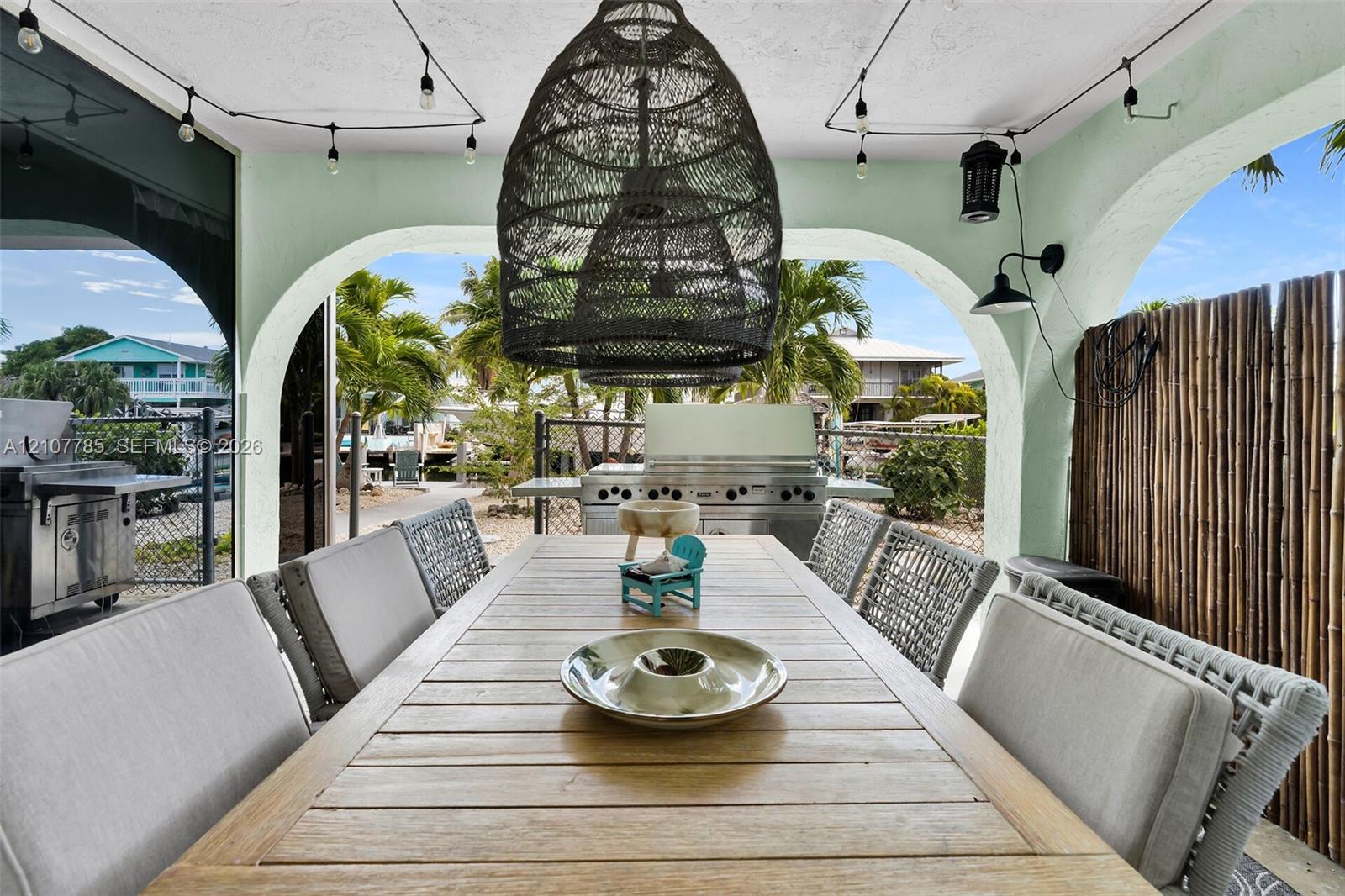 Covered outdoor living space featuring arched structural openings, built-in stainless steel grill, woven pendant light fixture, and mounted exterior wall sconces