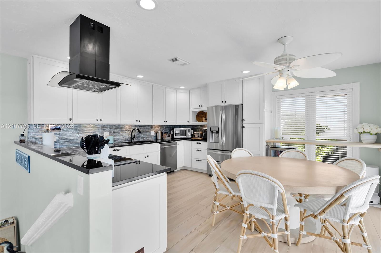Kitchen featuring white shaker-style cabinetry, dark stone countertops, a stainless steel refrigerator, a black wall-mounted range hood, and wood-finish flooring