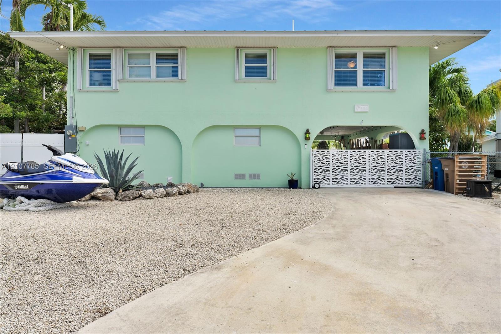 Two-story residence featuring architectural arched structural supports, a decorative metal privacy gate, concrete driveway, and low-maintenance gravel landscaping