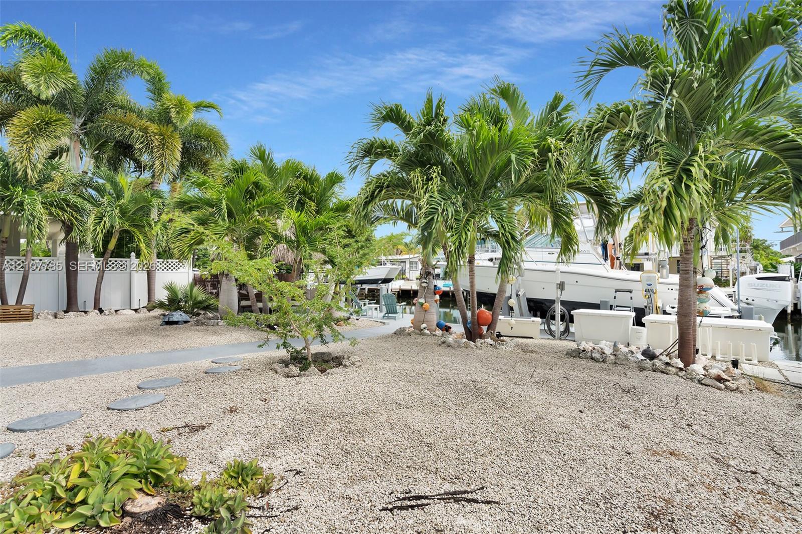 Waterfront exterior featuring a gravel landscape, mature palm trees, concrete walkway, and private boat dock