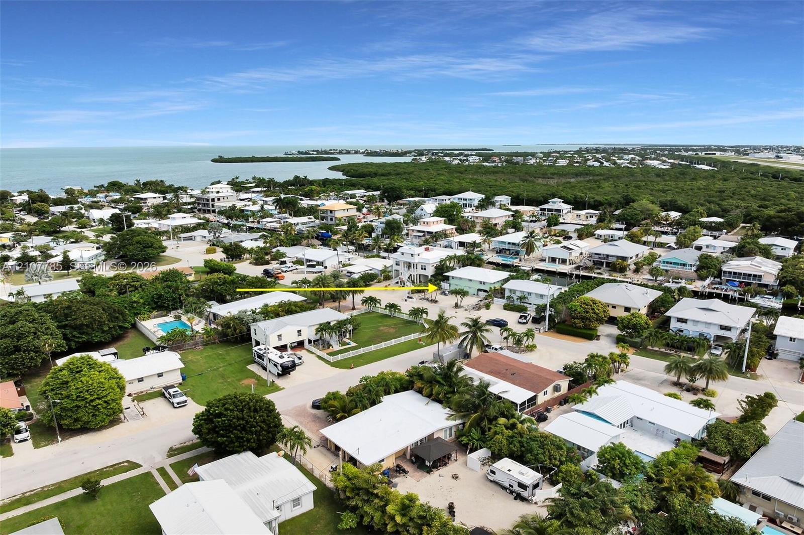 Aerial perspective of a coastal residential neighborhood featuring expansive water, proximity to protected natural areas, palm-dotted landscaping, and paved street infrastructure