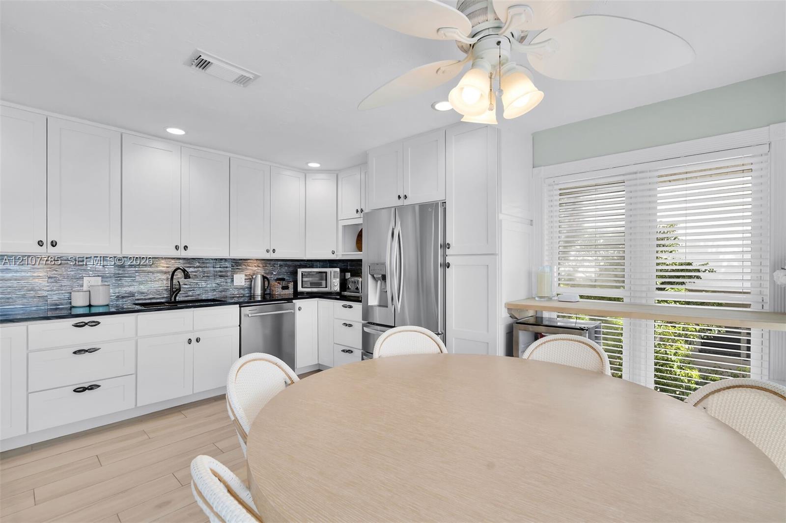 Kitchen featuring white shaker-style cabinetry, dark stone countertops, blue glass tile backsplash, stainless steel appliances, and wood-finish flooring
