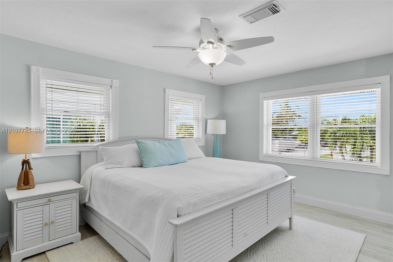 Bedroom featuring neutral wall paint, white wood-finish flooring, three windows with horizontal blinds, and a central ceiling fan with an integrated light fixture