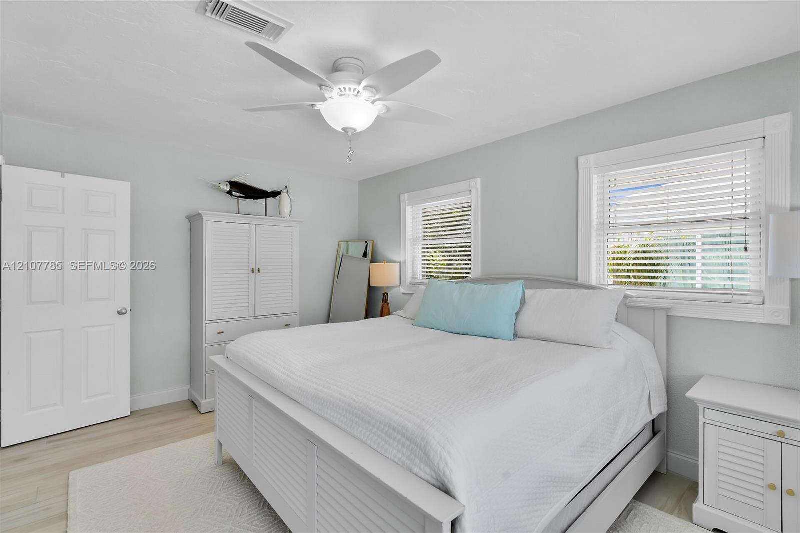 Light-filled room featuring wood-finish flooring, a white ceiling fan with integrated lighting, and dual windows with horizontal blinds
