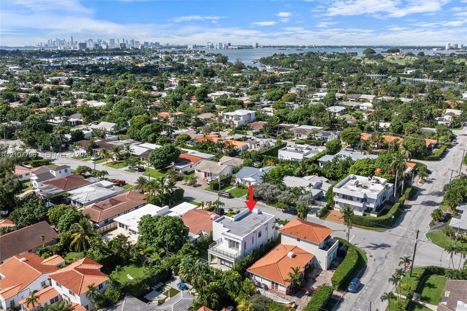 Aerial perspective of a multi-story residence featuring a flat roofline, an upper-level balcony with metal railings, and a fenced perimeter
