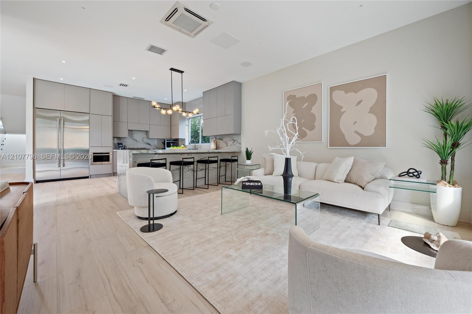 Modern kitchen and living area featuring wood-finish flooring, floor-to-ceiling cabinetry, a stone-surfaced waterfall edge island, and a multi-globe pendant light fixture