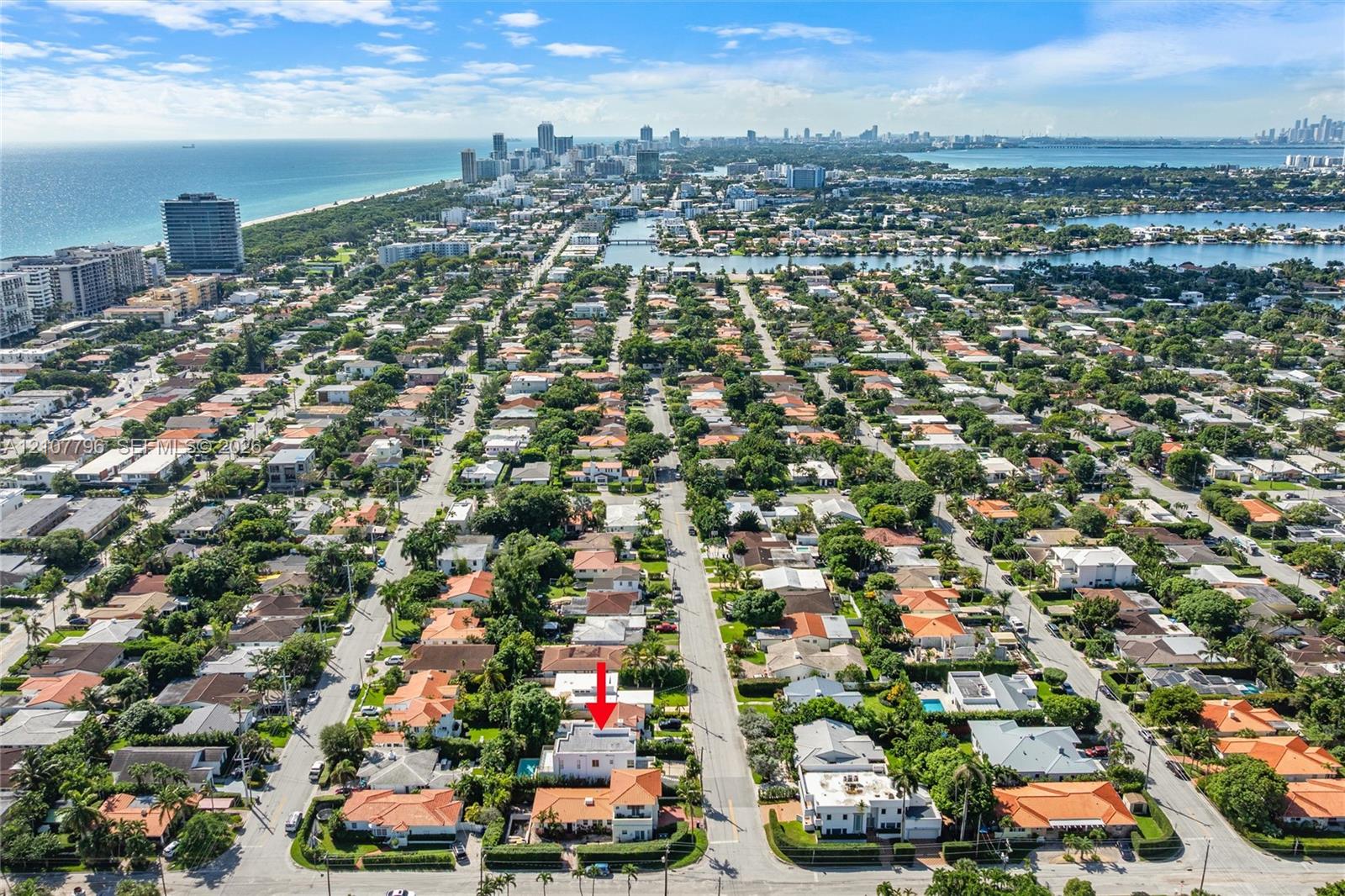 Aerial perspective showcasing a residential property with a swimming pool and multi-level roofline, situated within a coastal neighborhood near urban infrastructure and the shoreline