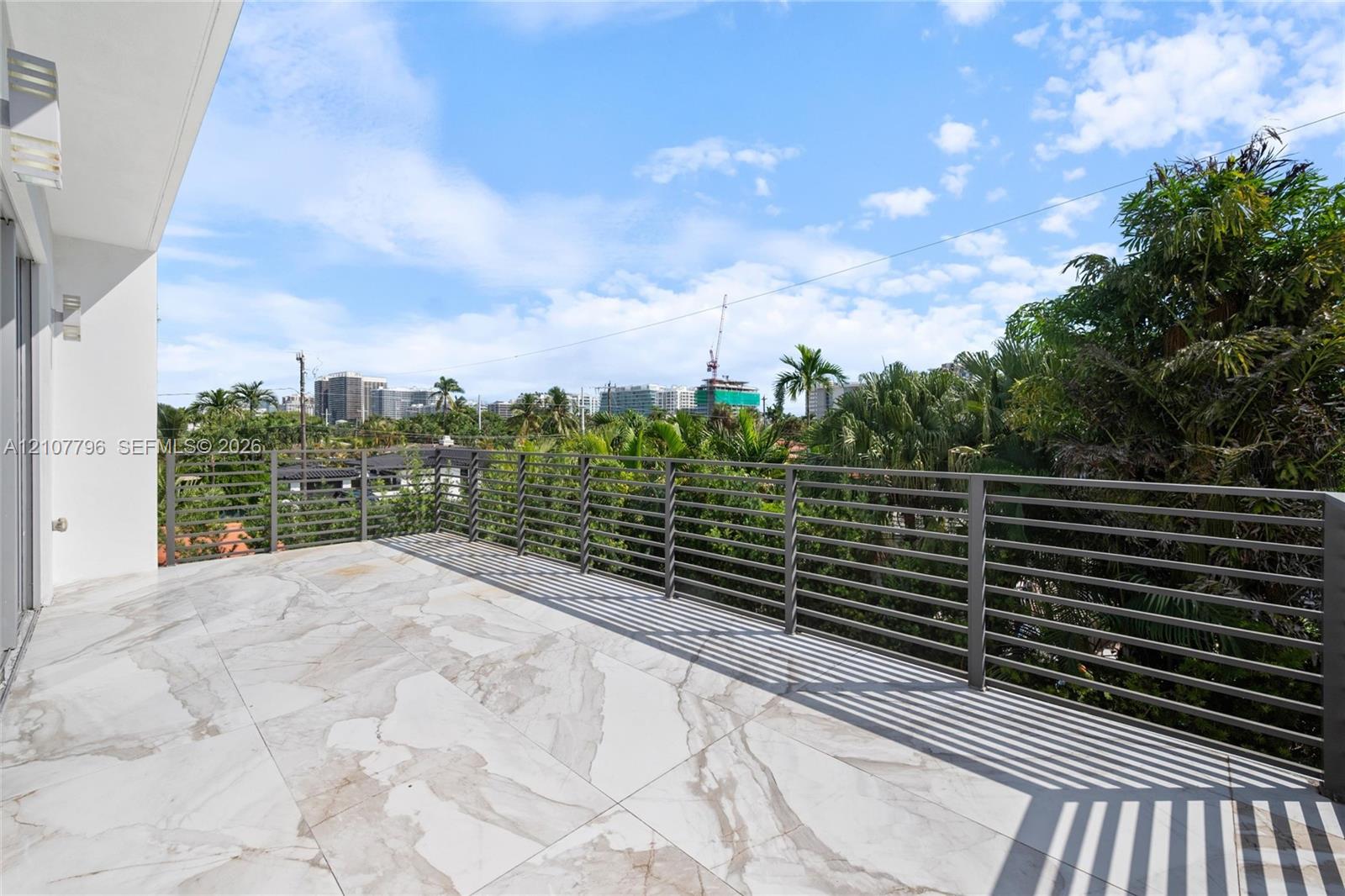 Expansive covered balcony featuring large-format stone-patterned tile flooring and a horizontal metal slat railing