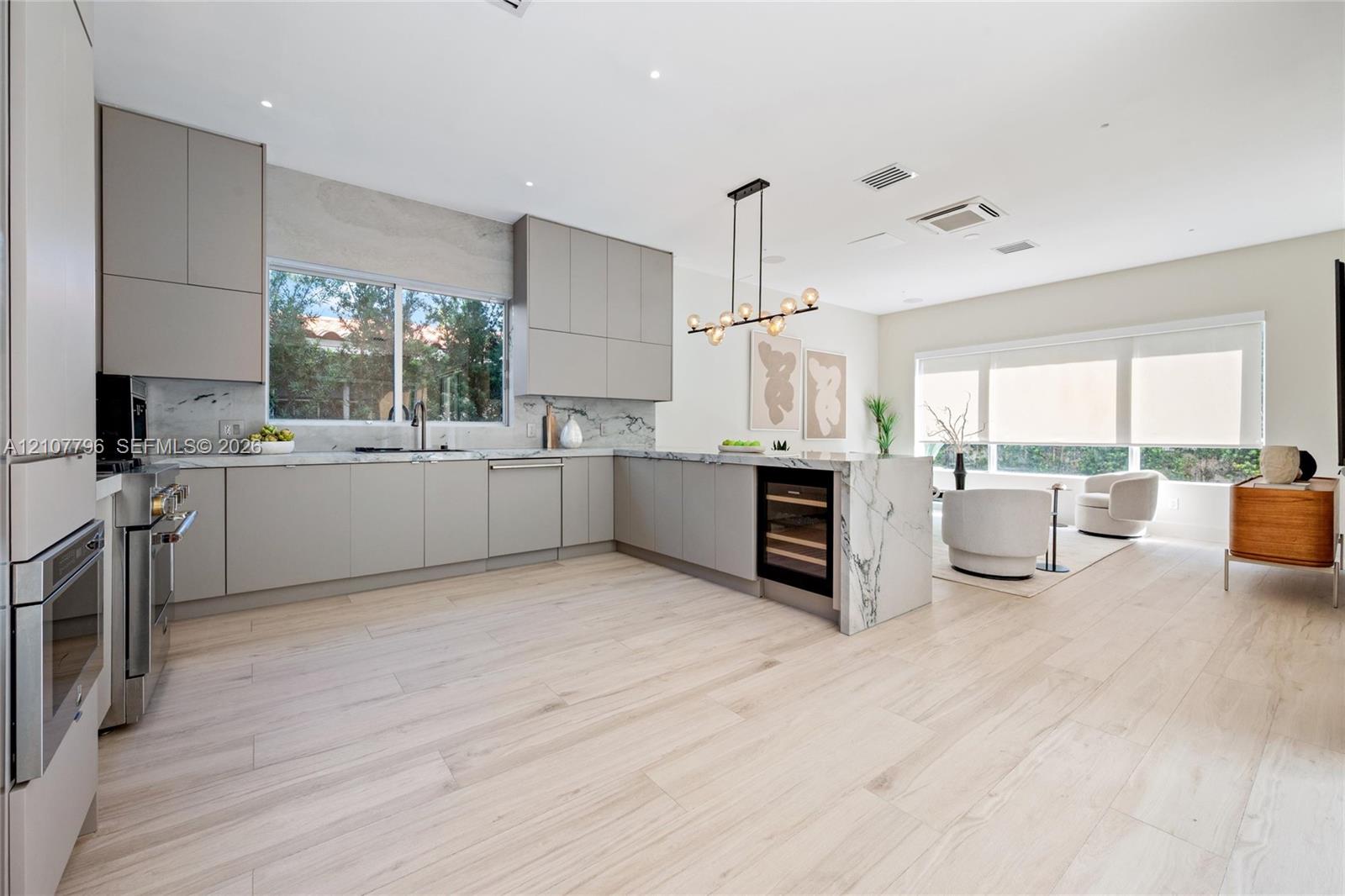Modern kitchen featuring flat-panel cabinetry, a waterfall-edge island, stone-finish backsplash, built-in wine refrigeration, and light-tone wood-finish flooring