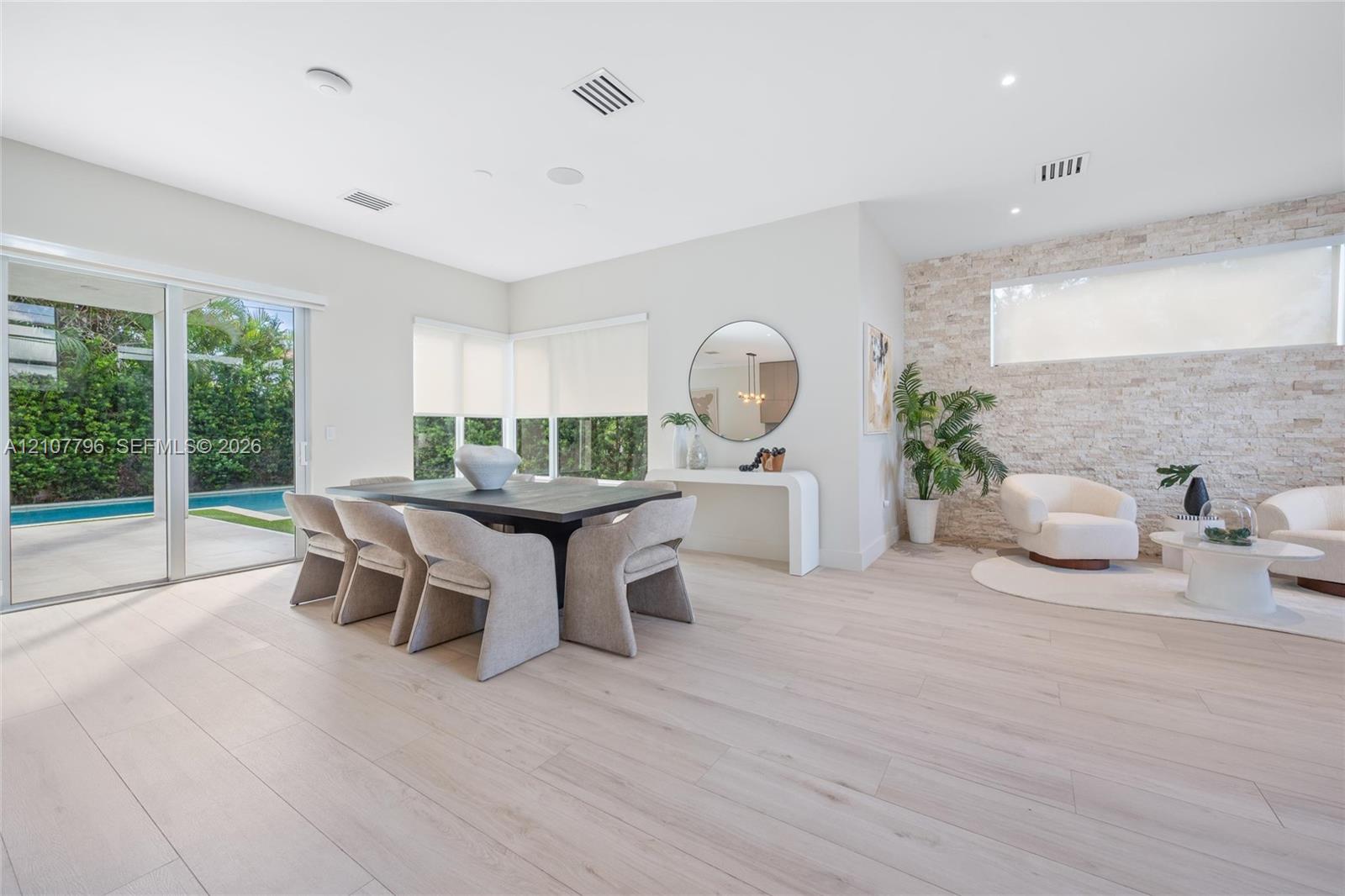 Open-concept living space featuring wood-finish flooring, a textured stone accent wall, recessed lighting, and large sliding glass doors providing outdoor access