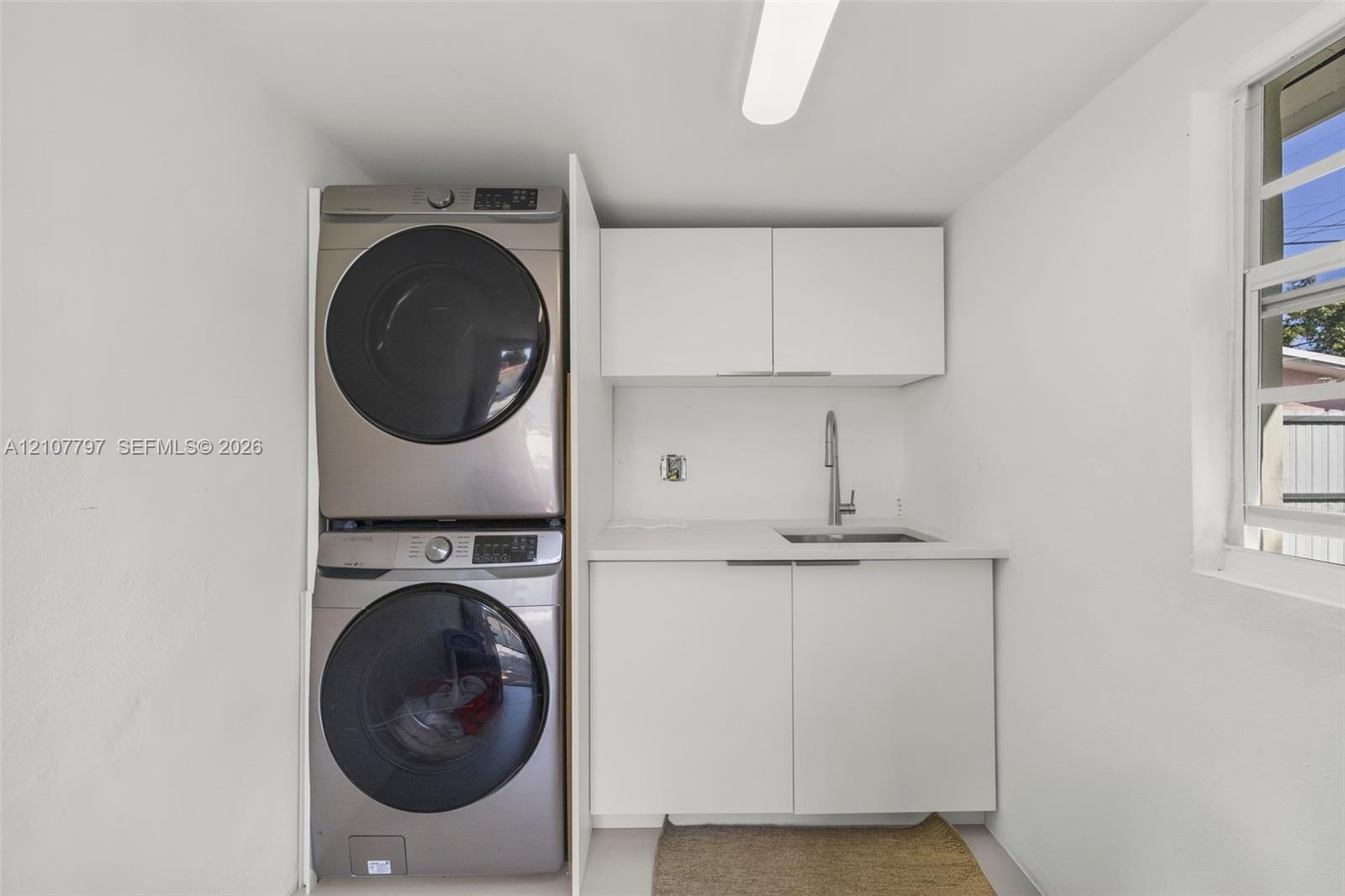 Laundry space featuring stacked front-load appliances, white cabinetry, a countertop with an integrated sink, and a gooseneck faucet