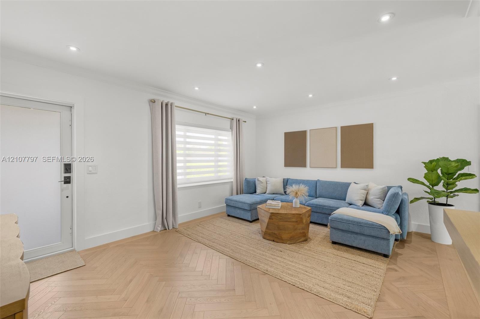 Living area featuring herringbone-patterned wood-finish flooring, recessed lighting, and a single-pane exterior door with a smart lock