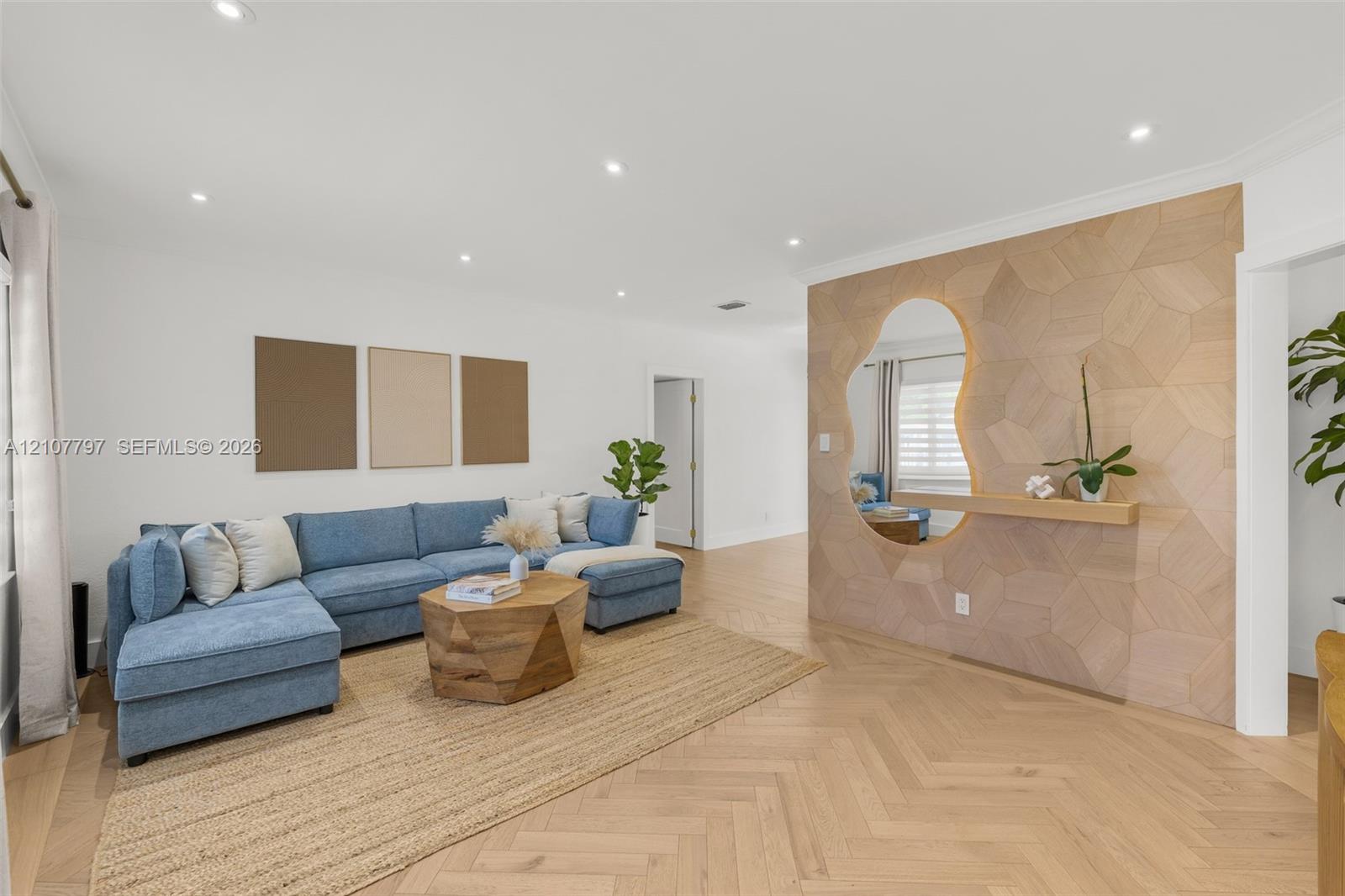 Herringbone wood-finish flooring, custom geometric wood-paneled accent wall, built-in floating shelf, organic-shaped wall mirror, and recessed lighting