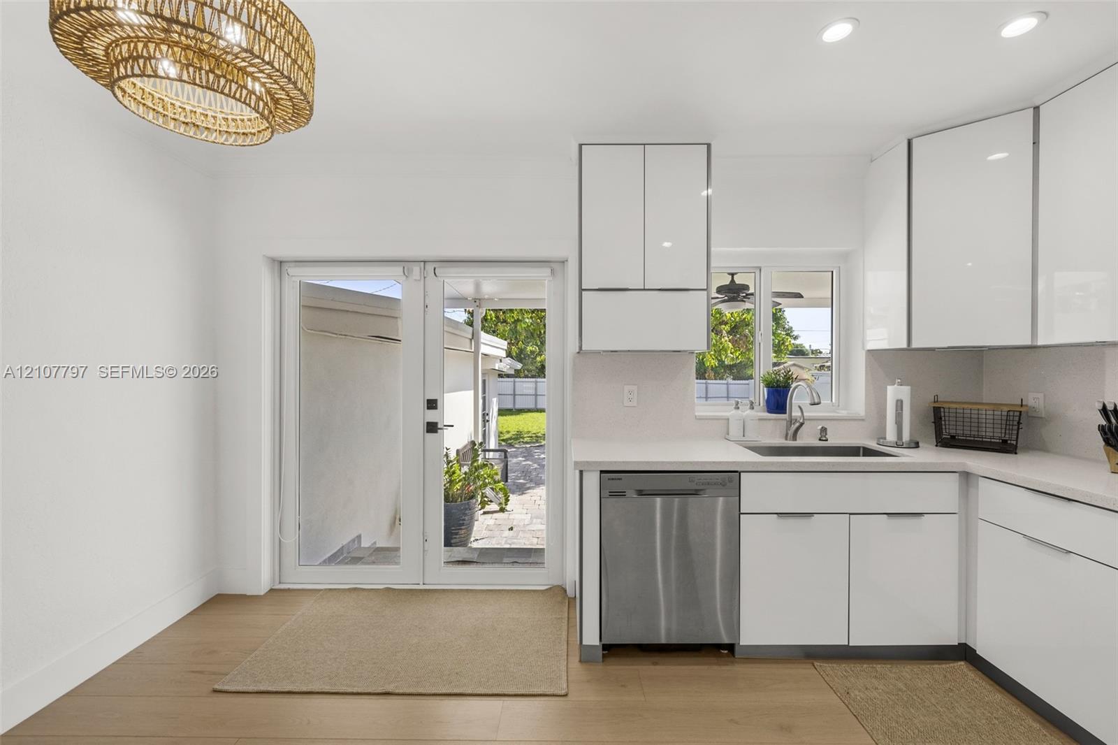 Kitchen featuring high-gloss white cabinetry, quartz countertops, stainless steel dishwasher, wood-finish flooring, and a textured woven light fixture