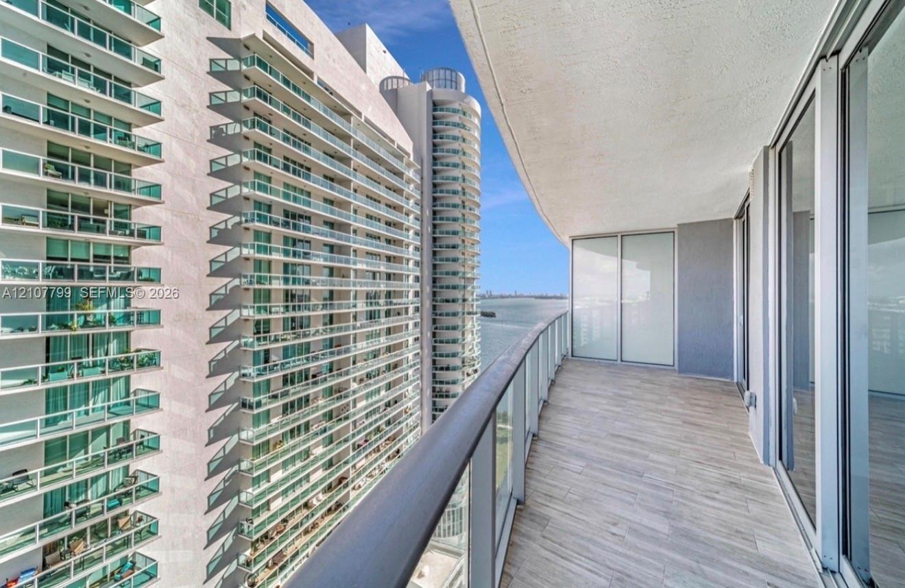Covered balcony featuring wood-finish flooring, glass panel railing, and full-height sliding glass doors