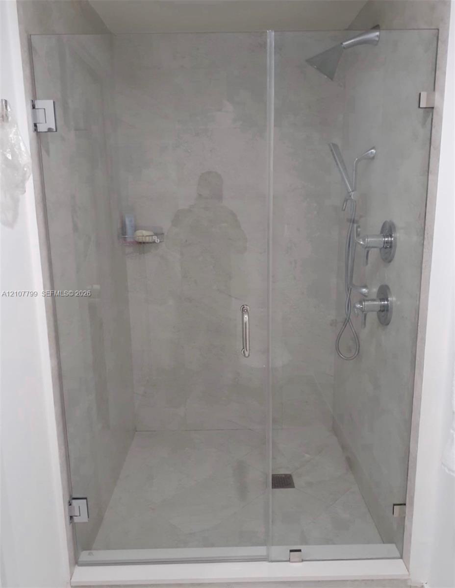 Walk-in shower featuring a frameless glass door, large-format tile surround, dual-head polished chrome shower system, and built-in corner shelving