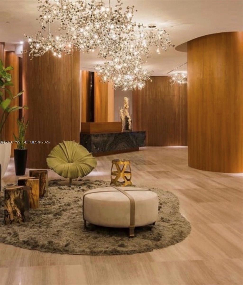 Interior foyer featuring curved wood-paneled walls, large-scale sculptural chandelier lighting, natural-finish stone flooring, and a stone-clad reception desk