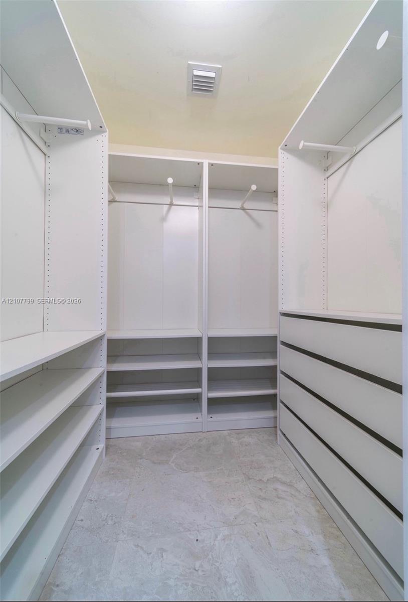 Custom walk-in closet featuring white built-in shelving, hanging rods, integrated drawer storage, and tile flooring