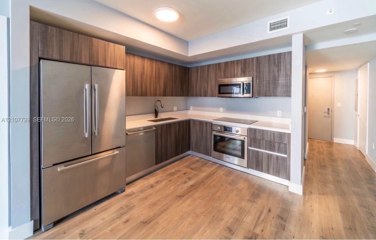 Modern kitchen featuring wood-finish cabinetry, stainless steel appliances, solid surface countertops, a matte black faucet, and wood-finish flooring