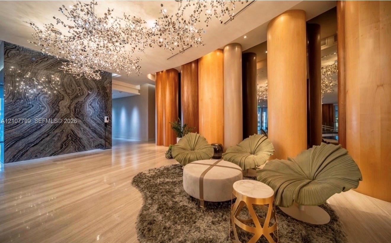 Large-scale sculptural chandelier, full-height decorative wood-paneled pillars, polished stone flooring, and expansive accent wall featuring dramatic natural veining