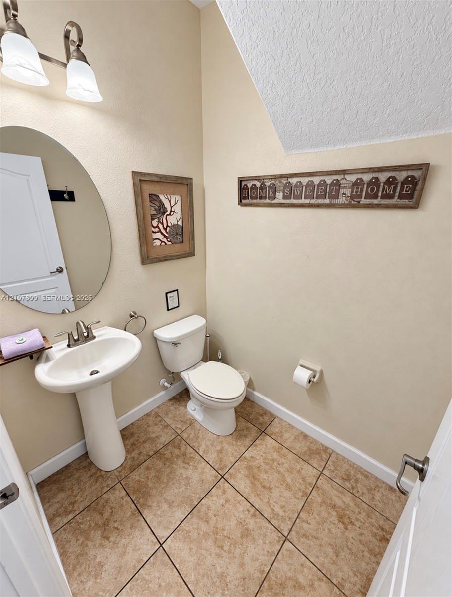 Pedestal sink with chrome faucet, oval wall-mounted mirror, two-light fixture with glass shades, and ceramic tile flooring