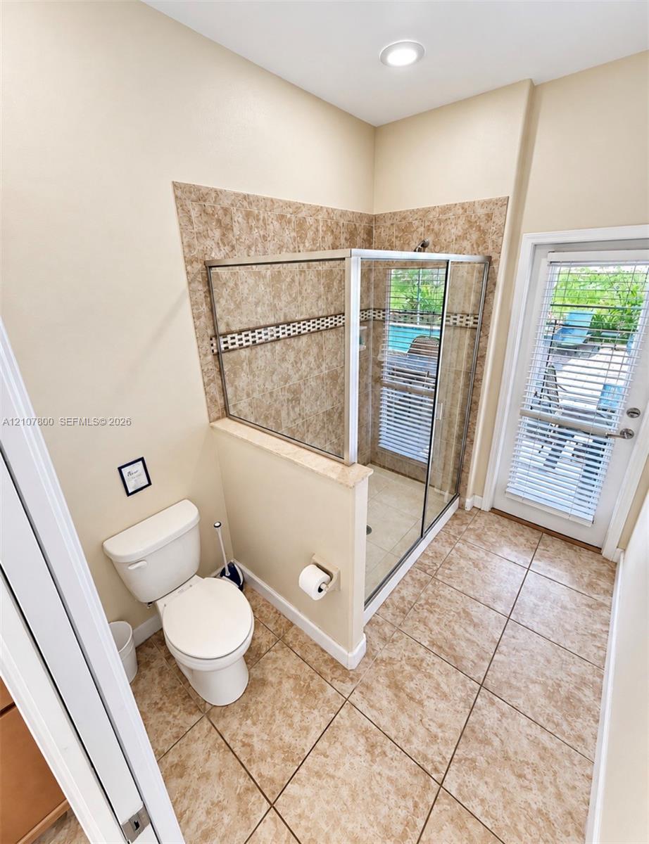 Enclosed glass-door shower featuring tile surround with decorative mosaic accent, ceramic tile flooring, recessed lighting, and a glass-paneled exterior door