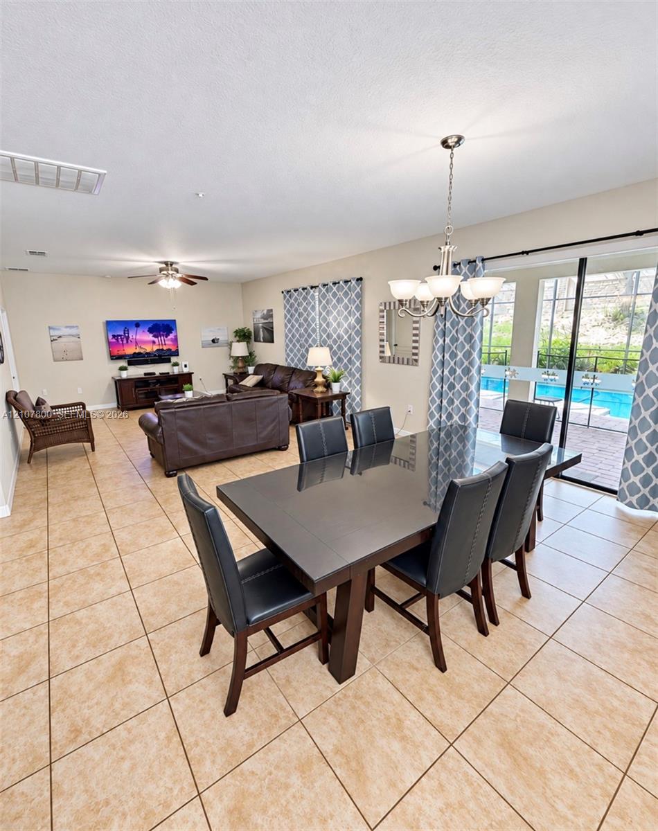 Open-concept interior featuring oversized tile flooring, a multi-arm chandelier, and sliding glass doors with direct exterior access to a pool
